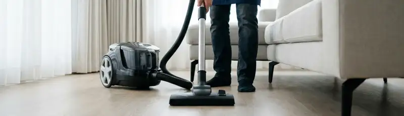 Professional house cleaner vacuuming a living room floor with a canister vacuum cleaner, Spokane, WA.