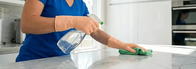 Maid service worker spraying and wiping a kitchen countertop with a microfiber cloth for sanitizing, Spokane, WA.