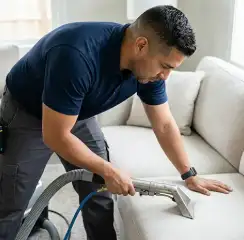 Professional upholstery cleaning technician using an extraction wand to deep-clean a fabric sofa, Spokane, WA.