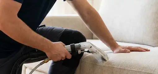 Professional upholstery cleaner deep-cleaning a fabric sofa with a handheld extraction tool, Spokane, WA.