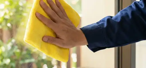 House cleaner wiping a glass window with a yellow microfiber cloth for streak-free cleaning, Spokane, WA.